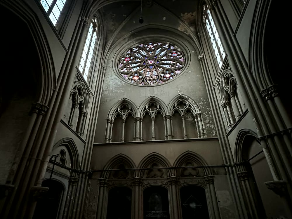 Abandoned church interior with stained glass and stone arches.